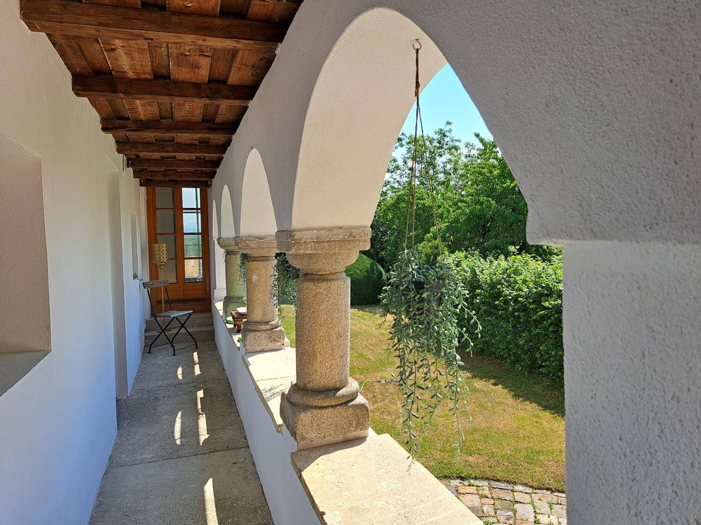 Überdachte Loggia mit Steinpfeilern und Blick auf den grünen Gartenbereich.