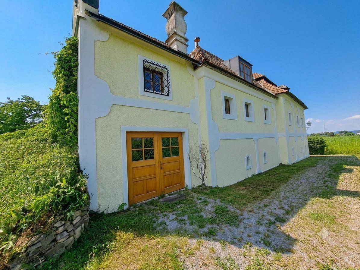 Historisches Gebäude mit gelber Fassade, Holztüren und umgeben von grüner Natur.