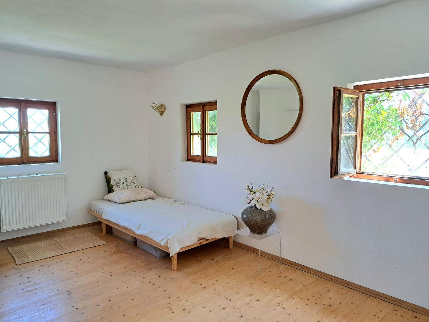 Helles Schlafzimmer mit Holzboden, Einzelbett und mehreren Fenstern.