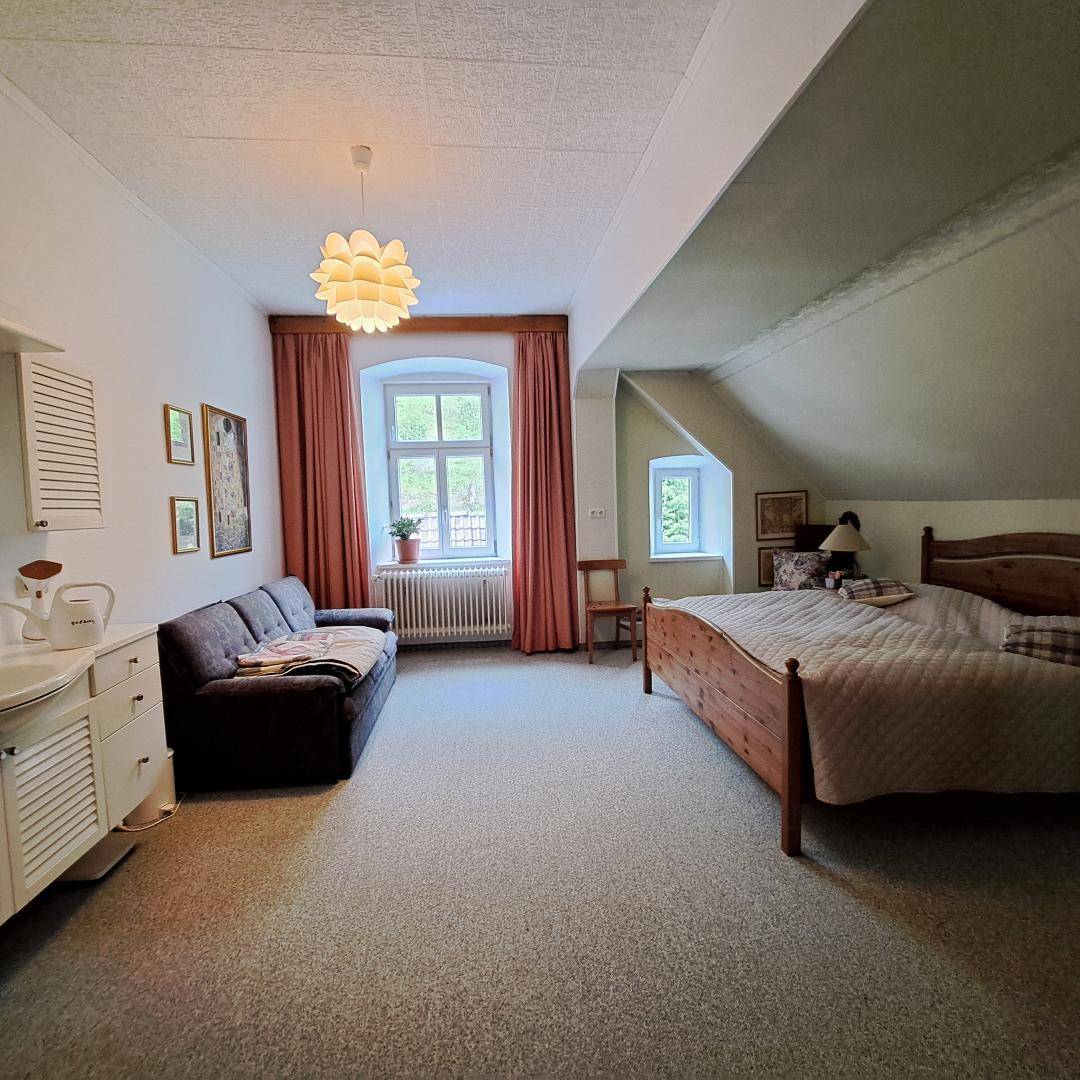 Helles Schlafzimmer mit Holzbett, Sofa und schrägen Decken, ideal als Gästezimmer.