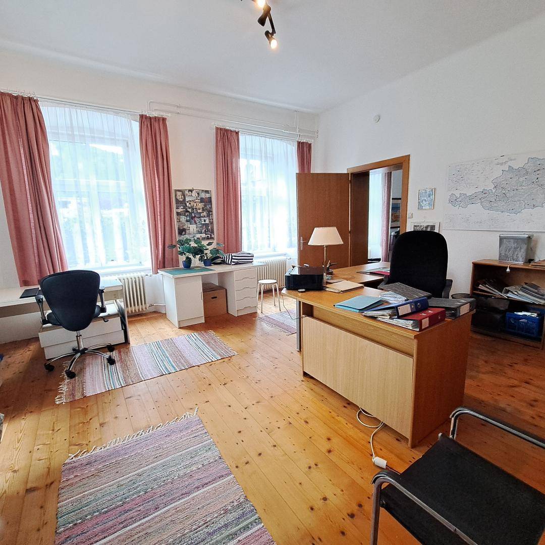 Helles Büro mit Holzboden, zwei Schreibtischen und großen Fenstern, ideal zum Arbeiten.