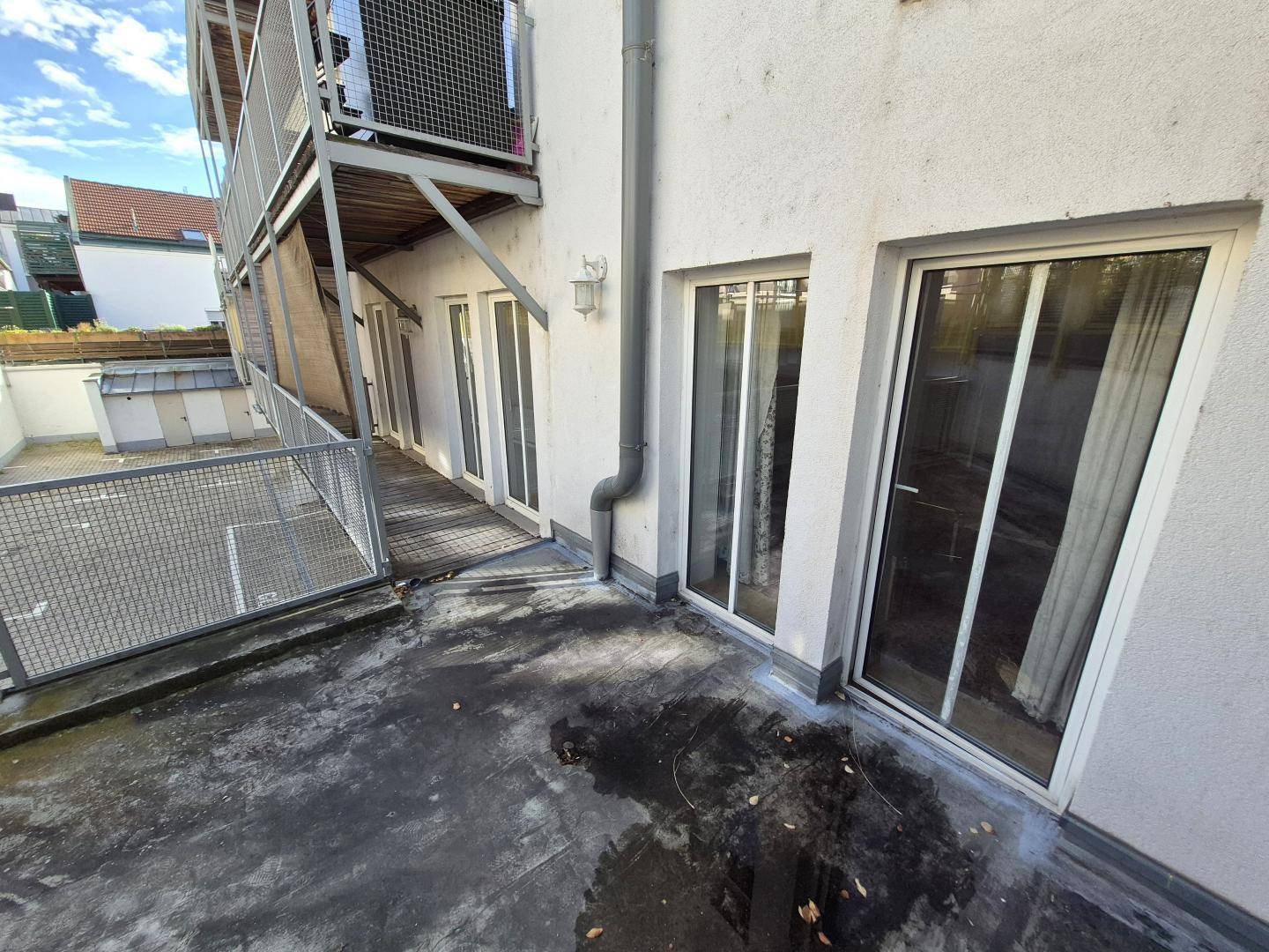 Außenbereich mit Metallbalkon und mehreren Fenstertüren, die Zugang zu den Wohneinheiten bieten.