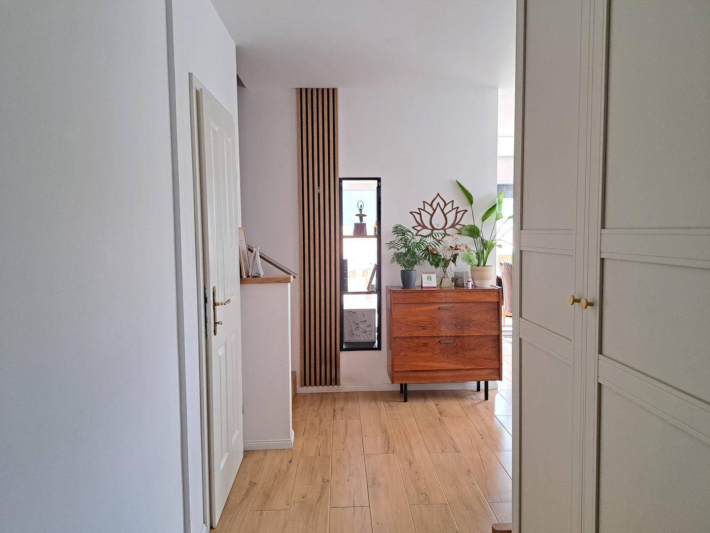 Heller Flur mit Holzfußboden, einer Kommode und dekorativen Holzelementen an der Wand.