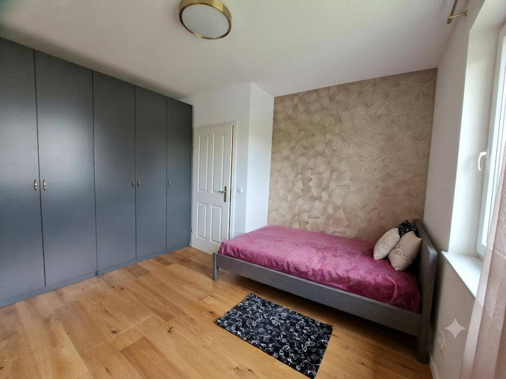 Schlafzimmer mit Einzelbett, grauen Einbauschränken und einer strukturierten Akzentwand.