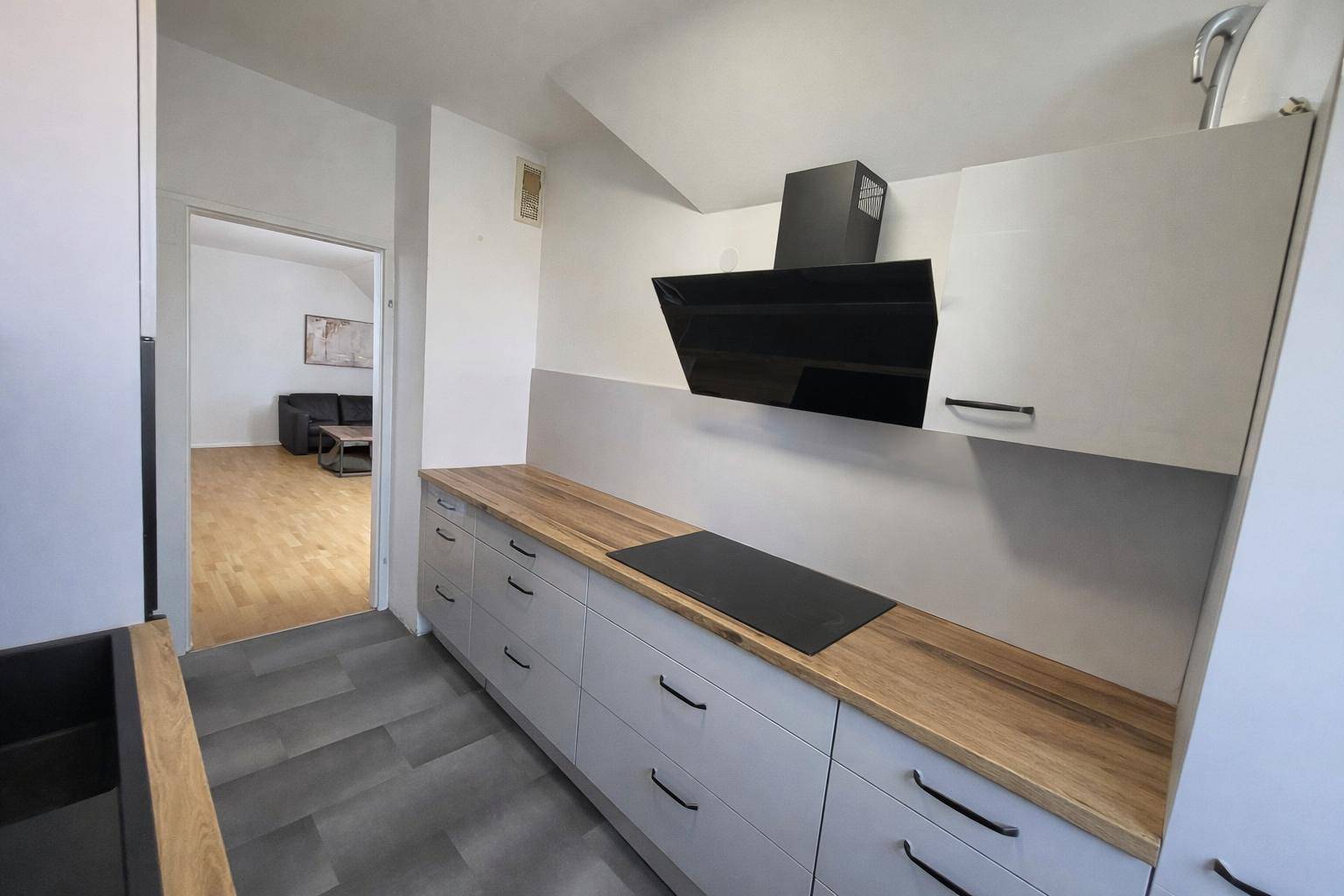 Moderne Küche mit Holz-Arbeitsplatte, Induktionskochfeld und einer eleganten Dunstabzugshaube.