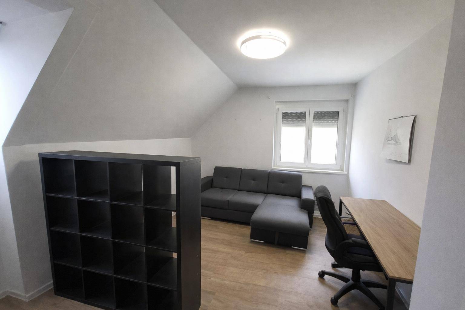 Dachgeschosszimmer mit Schreibtisch, Sofa und einem praktischen Stauraumregal.
