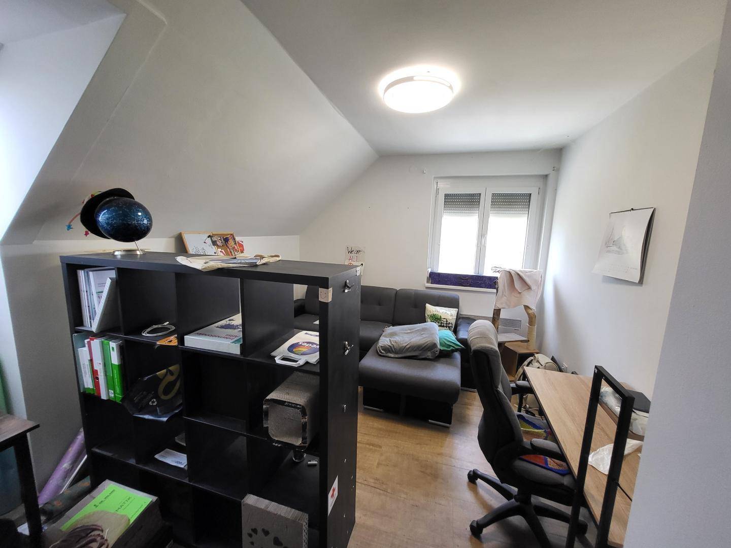 Helles Dachgeschosszimmer mit Regal, Sofa und einem funktionalen Arbeitsbereich.