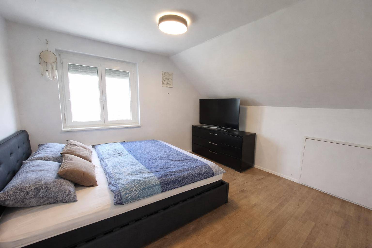 Gemütliches Schlafzimmer im Dachgeschoss mit Bett, Fernseher und schrägen Wänden.