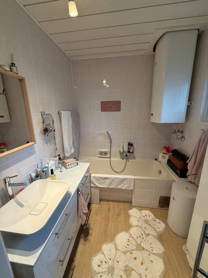 Badezimmer mit Badewanne, modernem Waschbecken, hellen Fliesen und Laminatboden.