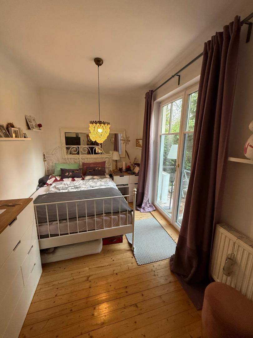 Schlafzimmer mit Holzdielenboden, einem weißen Metallbett und Zugang zu einem Außenbereich.