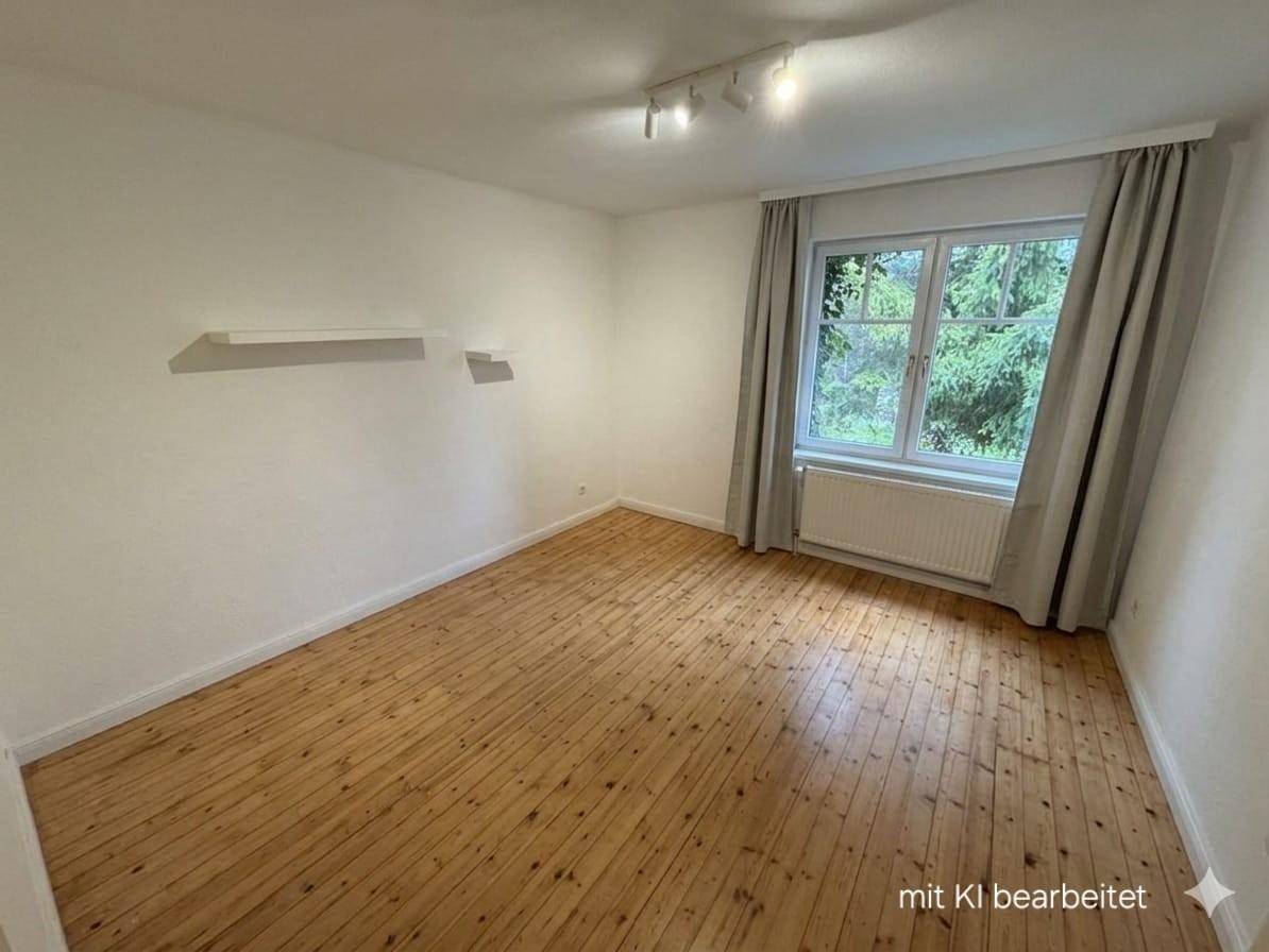 Leerer Raum mit Holzdielenboden, einem Fenster mit grauen Vorhängen und einer Wandablage.