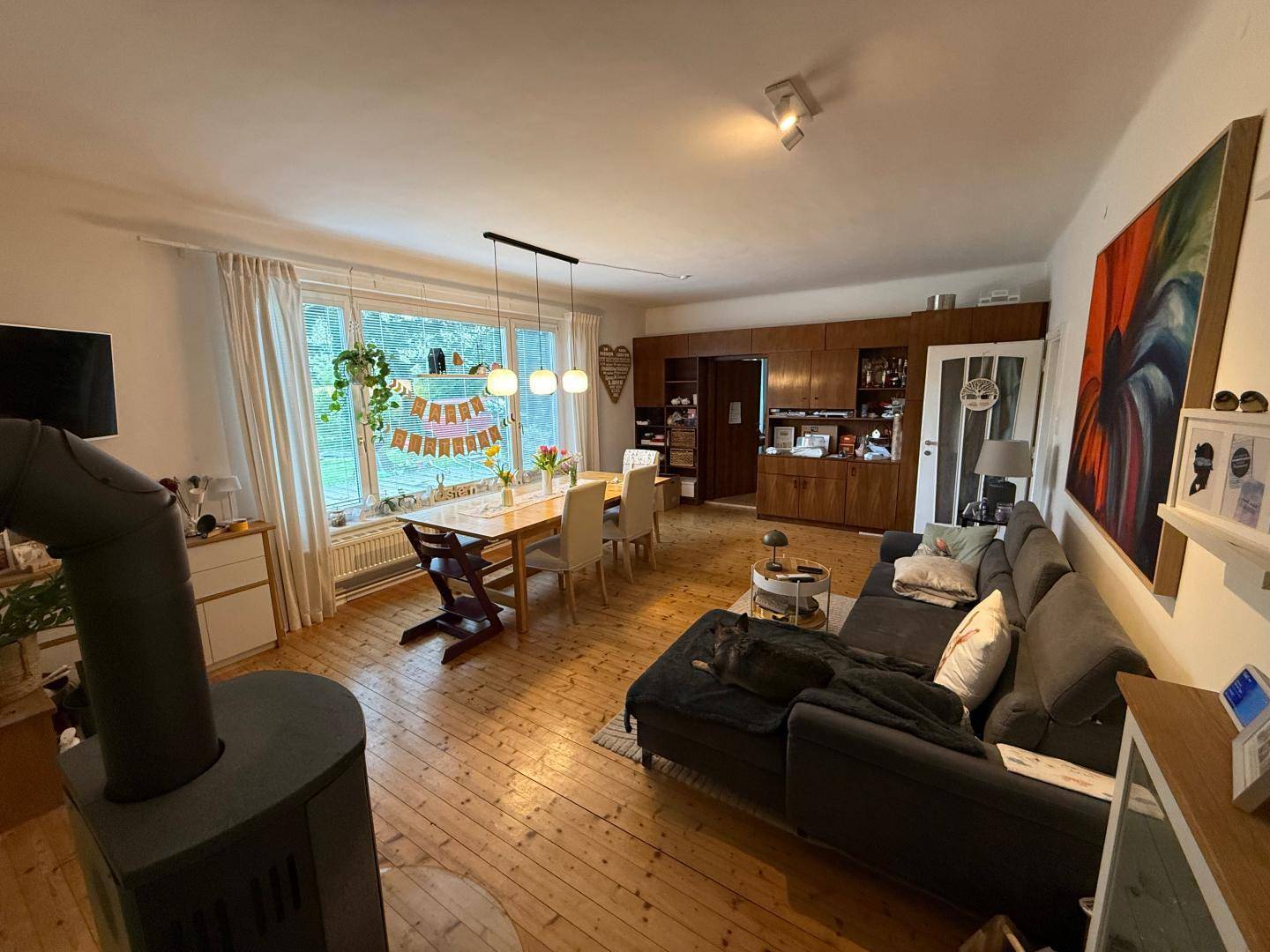 Geräumiger Wohn-Essbereich mit Holzboden, Einbauschränken und einem modernen Holzofen.