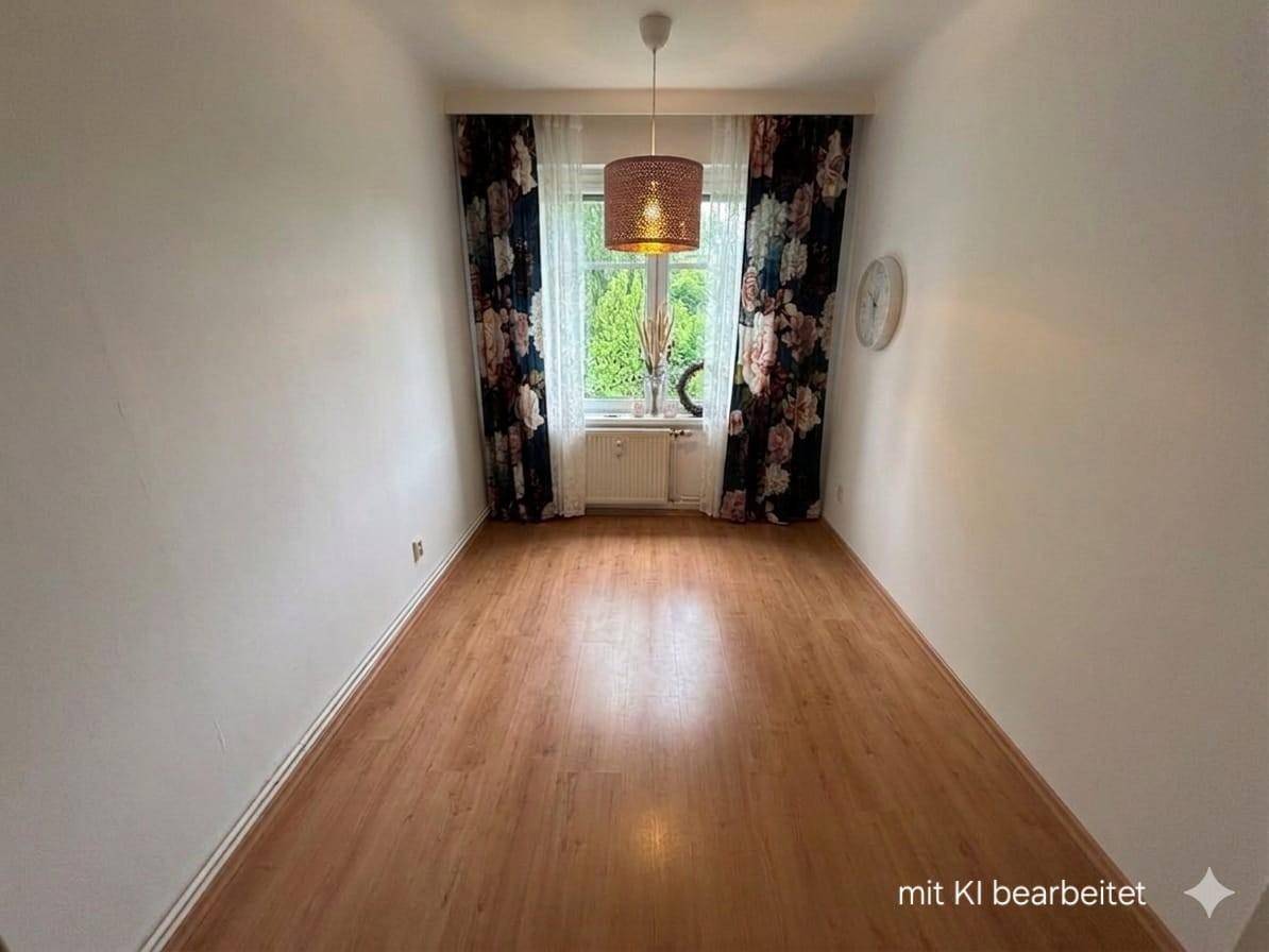 Leerer Raum mit Laminatboden und einem Fenster mit gemusterten Vorhängen.