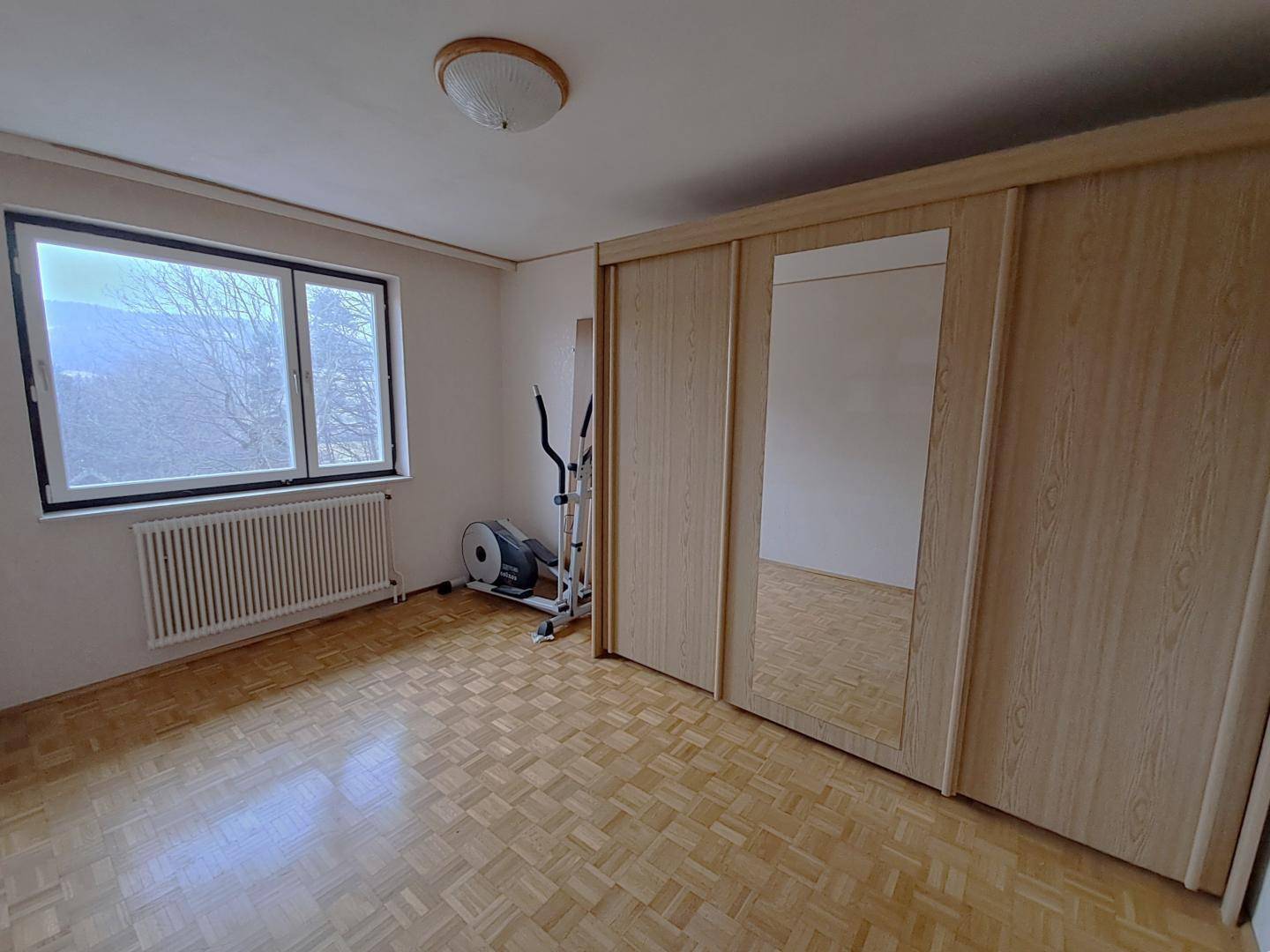 Schlafzimmer mit Parkettboden, großem Fenster und Einbauschränken mit Spiegelfronten.