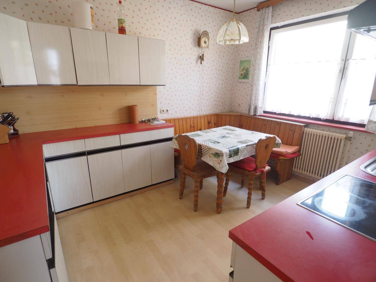 Traditionelle Küche mit roten Arbeitsplatten, Holzelementen und einer gemütlichen Essecke am Fenster.