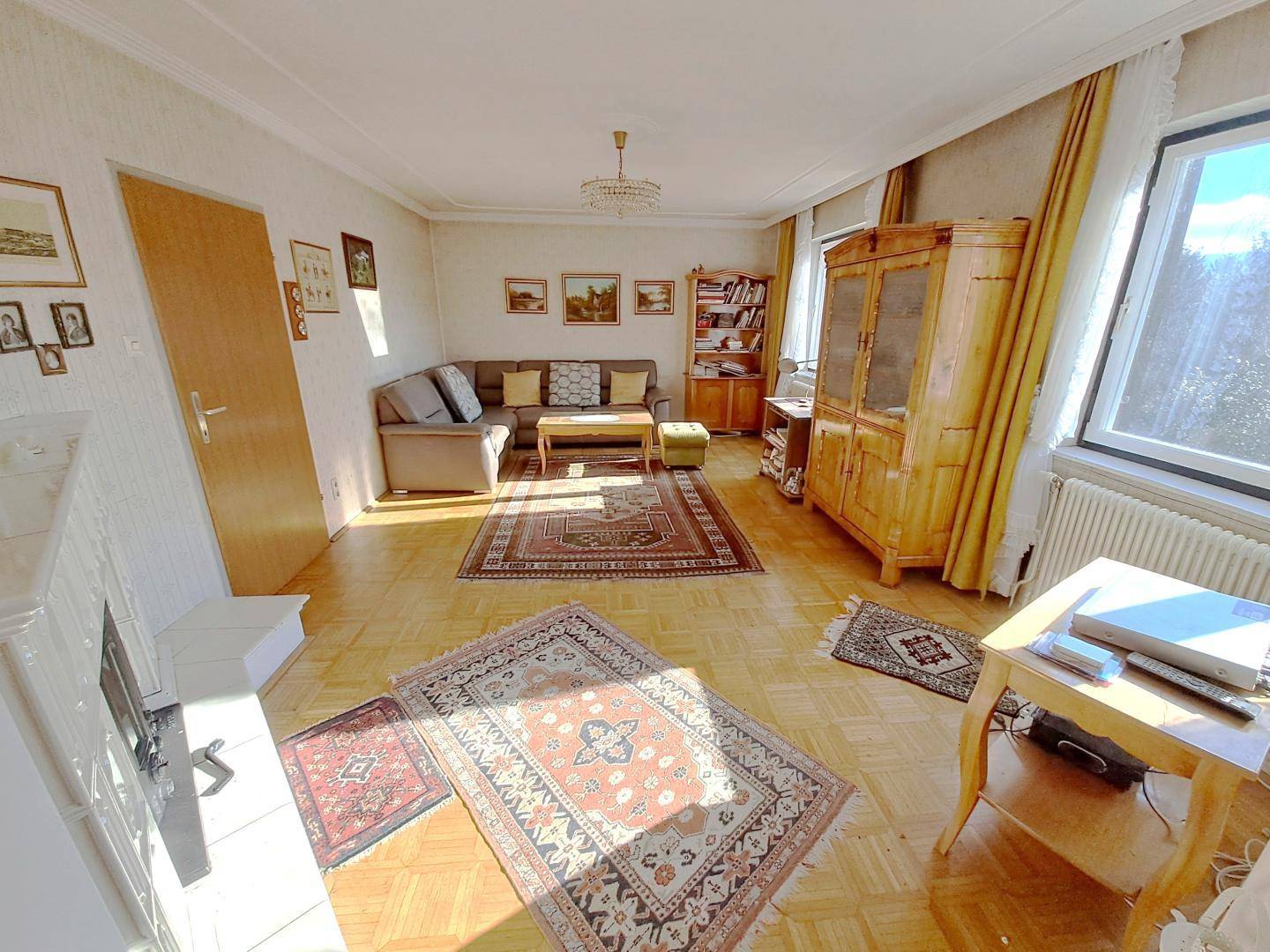 Helles Wohnzimmer mit Parkettboden, gemütlicher Sitzecke und traditionellem Holzschrank.