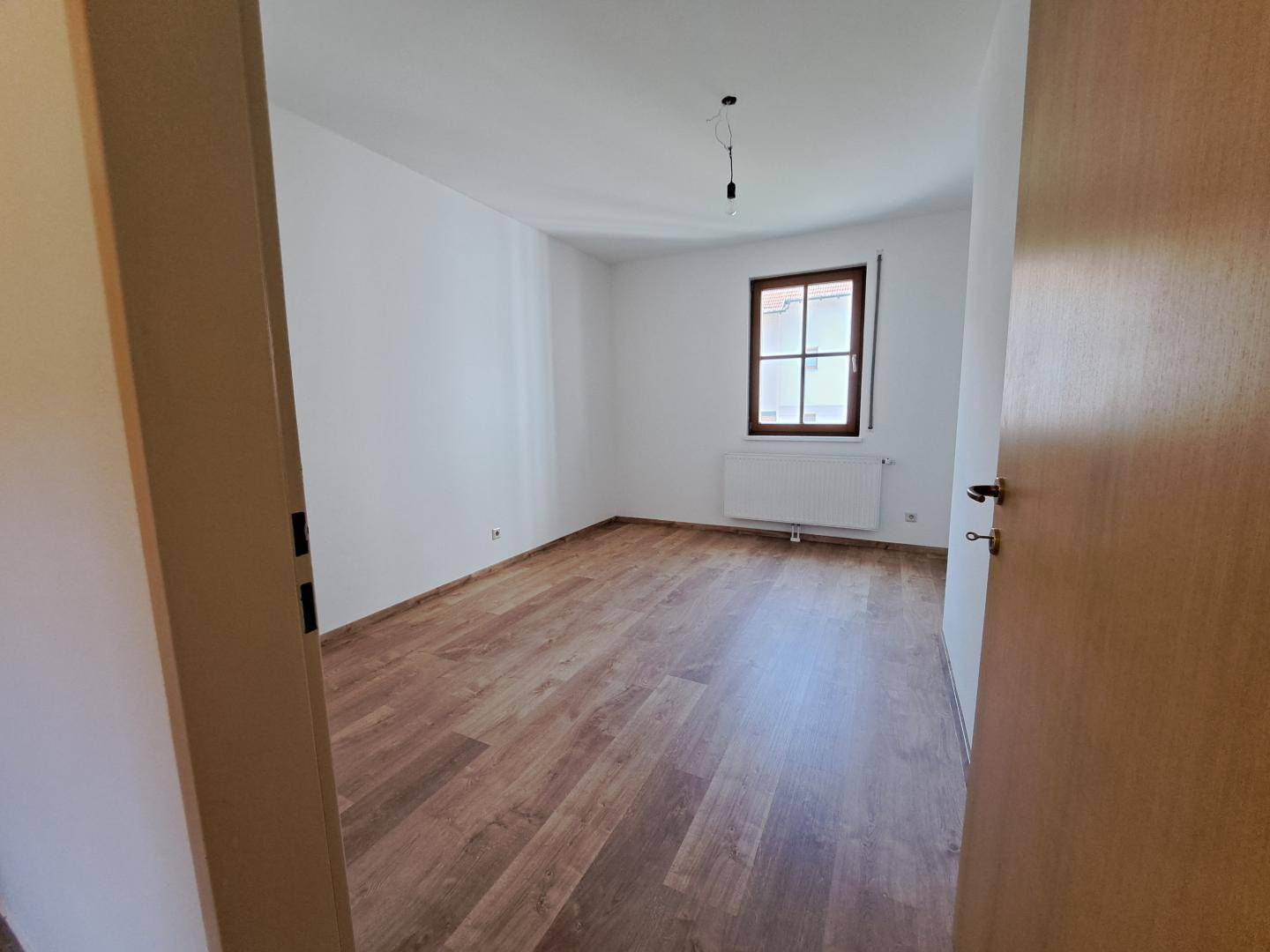 Leeres Schlafzimmer mit Laminatboden und Fenster, ideal für persönliche Einrichtung.