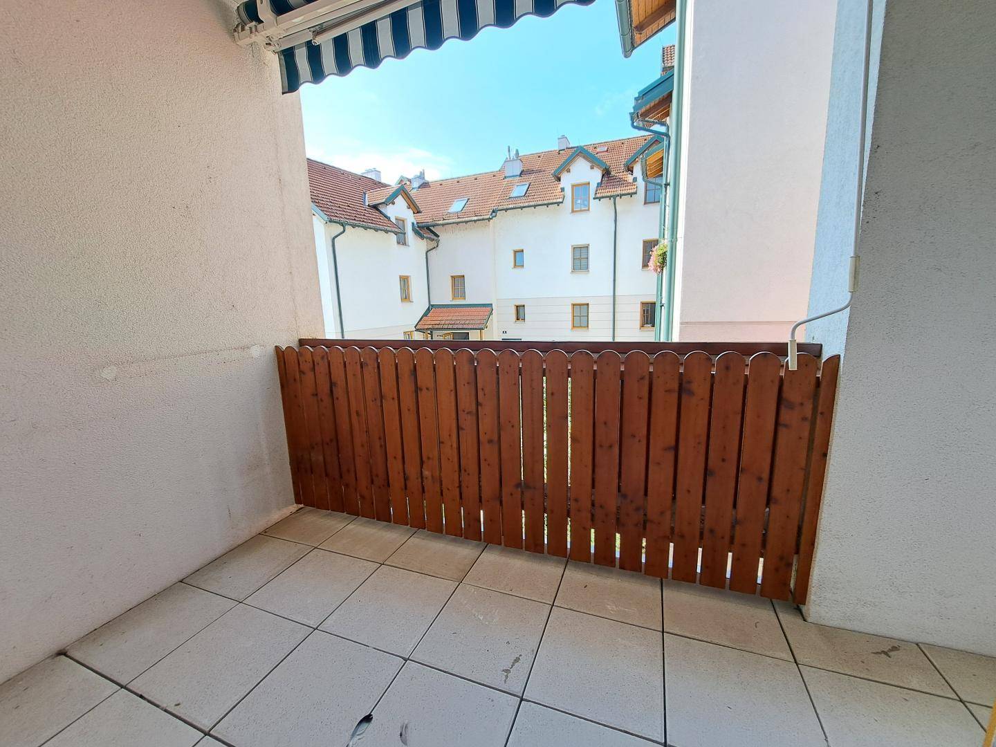 Kleiner Balkon mit Fliesenboden und Holzzaun, mit Blick auf umliegende Gebäude.