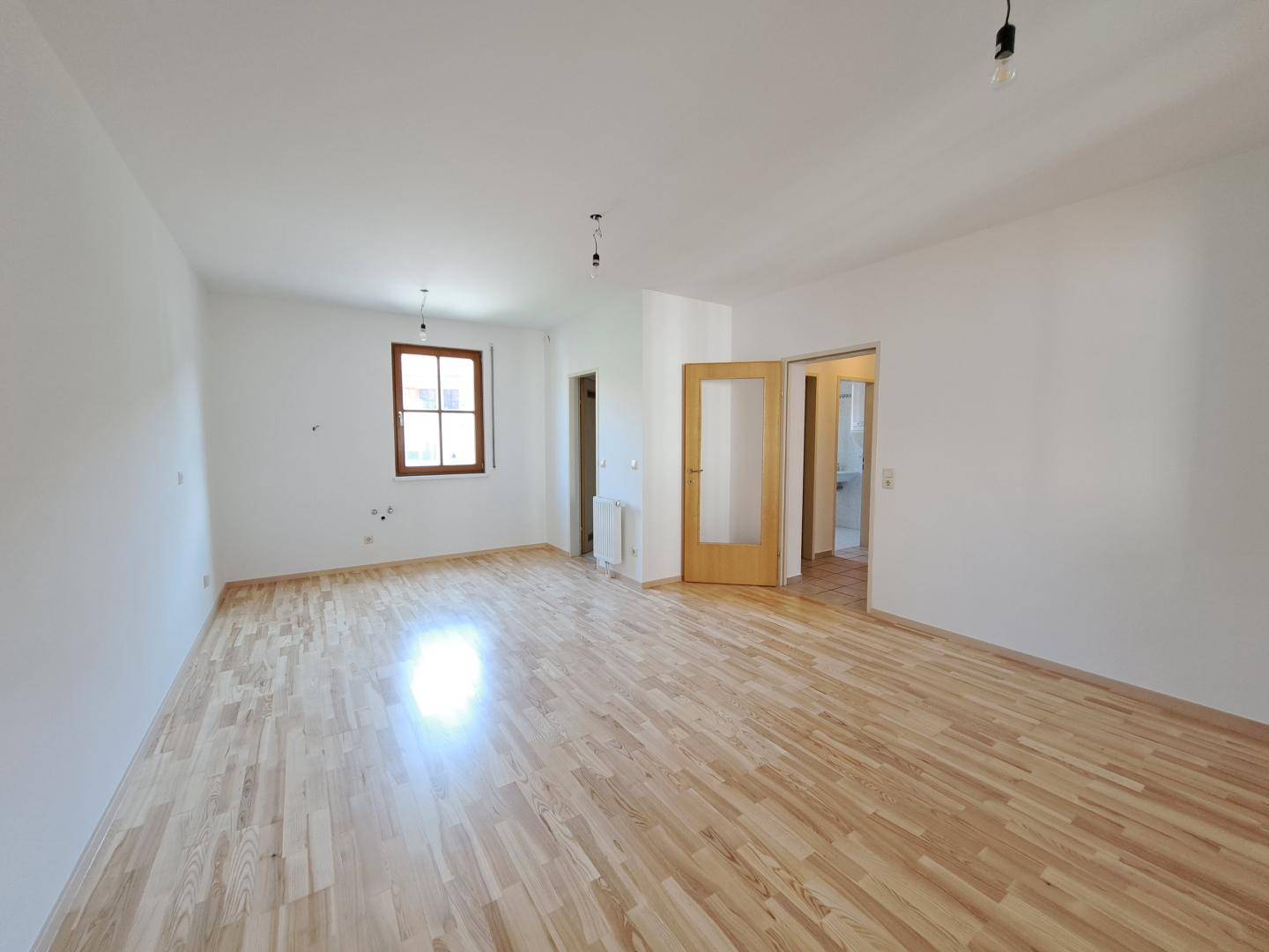 Geräumiger, heller Raum mit Holzboden und Fenster, bereit zur individuellen Gestaltung.