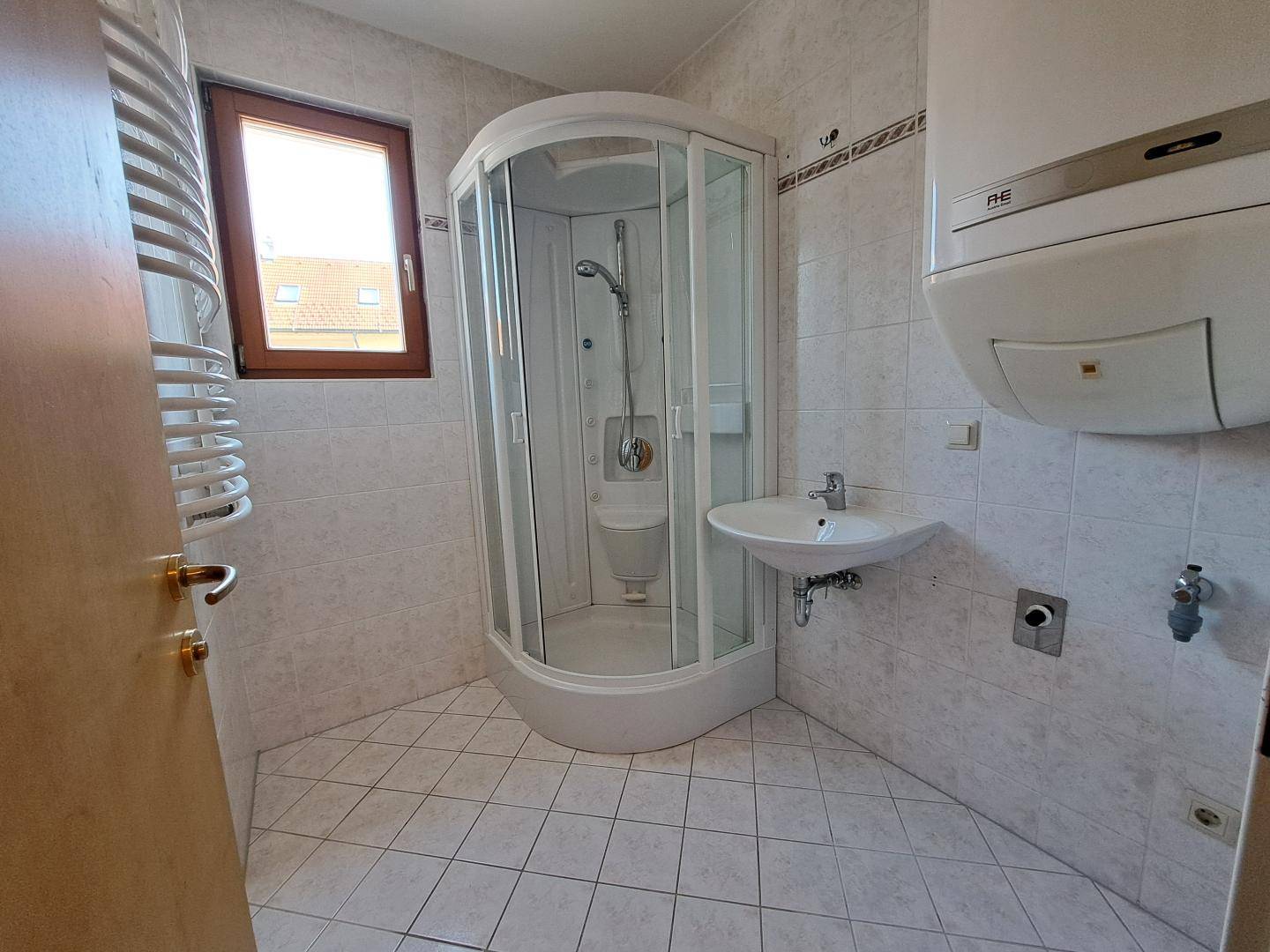 Badezimmer mit Duschkabine, Waschbecken und Fenster, hell gefliest.