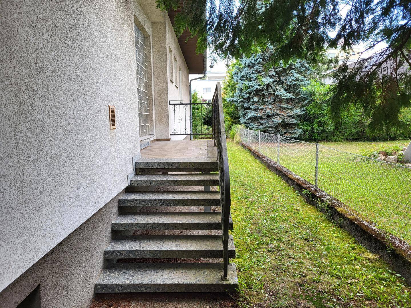 Außentreppe führt zu einem Eingangsbereich, umgeben von einem eingezäunten Gartenbereich.