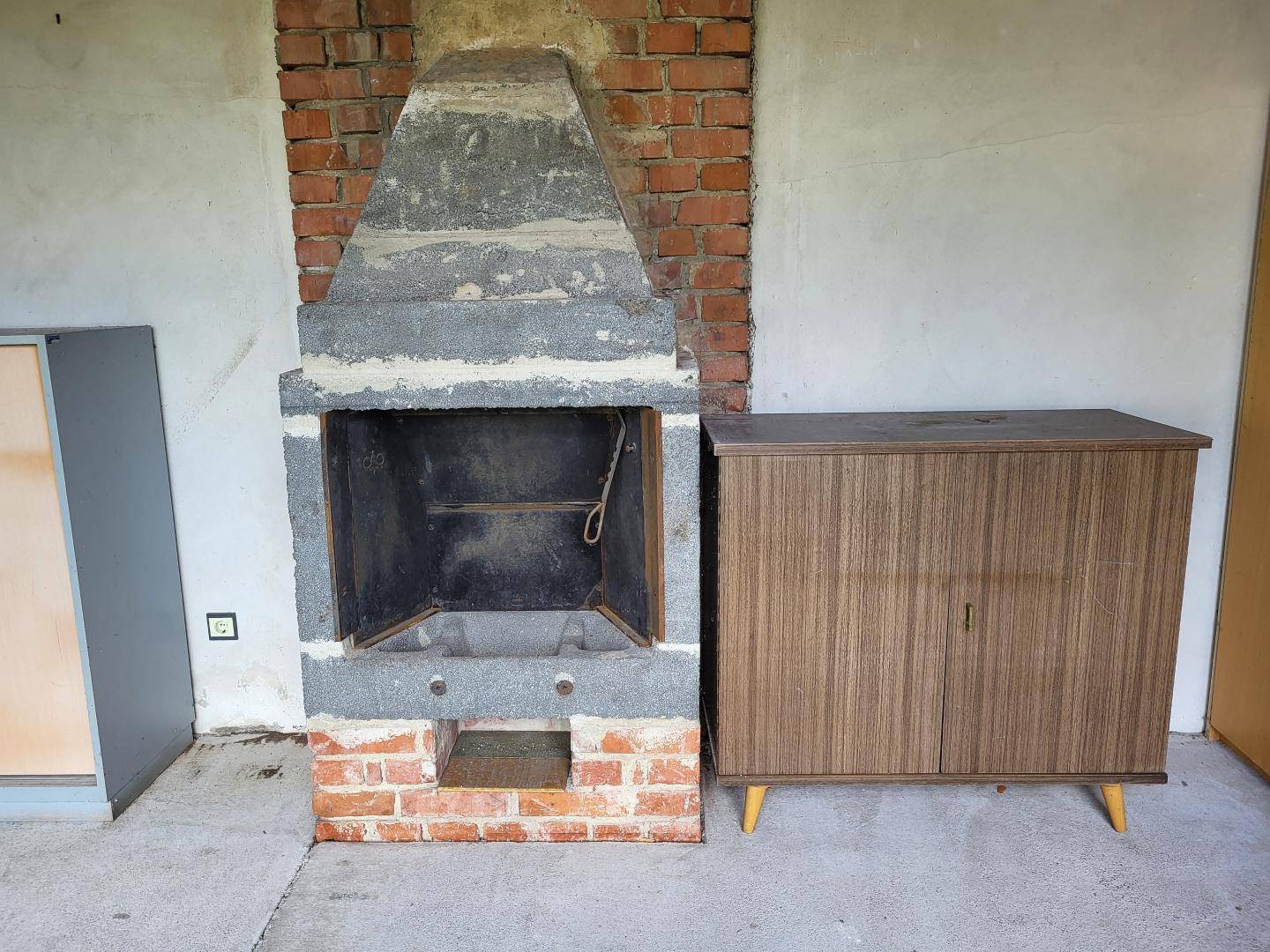 Außenkamin oder Grillplatz aus Stein und Ziegeln mit einem Holzschrank daneben.
