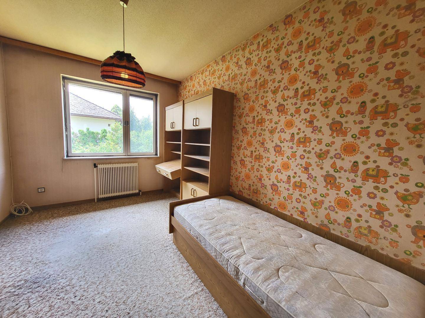 Kinderzimmer mit gemusterten Tapeten, Teppichboden und einem Einzelbett.