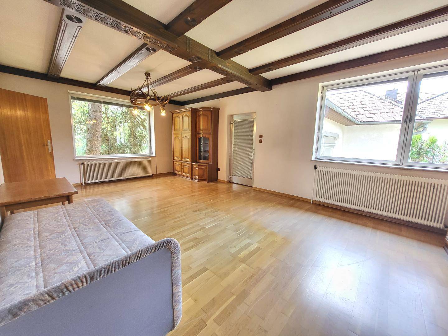 Geräumiges Wohnzimmer mit Holzbalkendecke, Parkettboden und großen Fenstern.