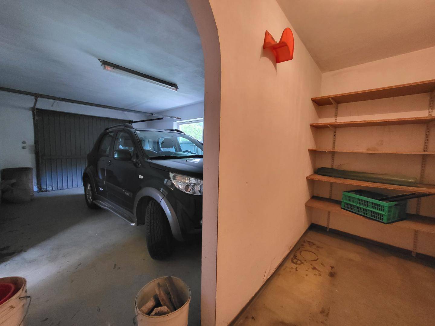 Garage mit Platz für ein Fahrzeug und zusätzlichen Regalen für Stauraum.