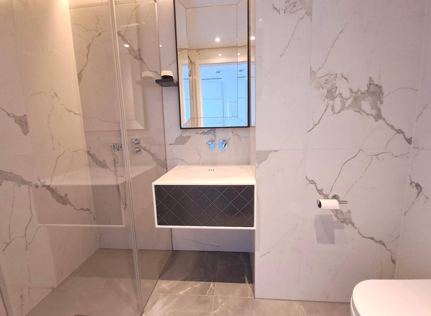 Modernes Badezimmer mit Marmorfliesen, begehbarer Dusche und schwebendem Waschtisch.