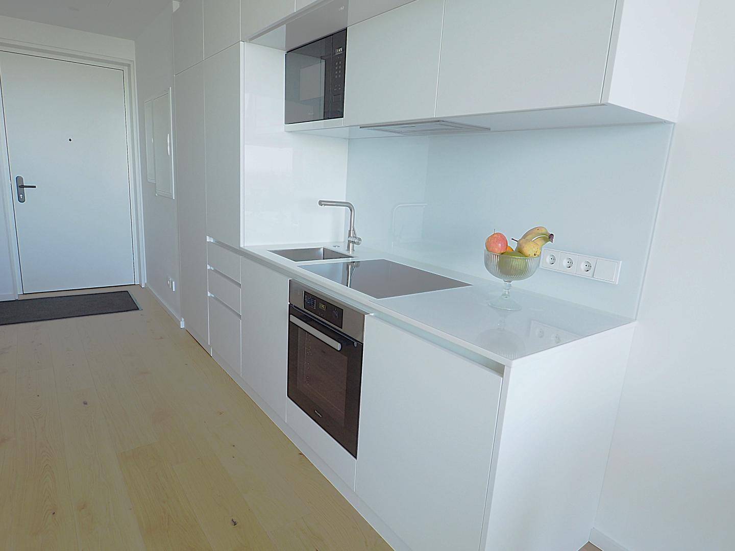 Moderne Küchenzeile mit weißen Hochglanzfronten, Induktionskochfeld und integriertem Backofen.