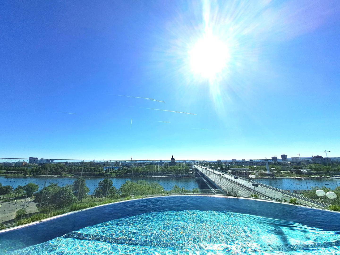 Infinity-Pool mit spektakulärem Panoramablick über die Stadt und den Fluss an einem sonnigen Tag.