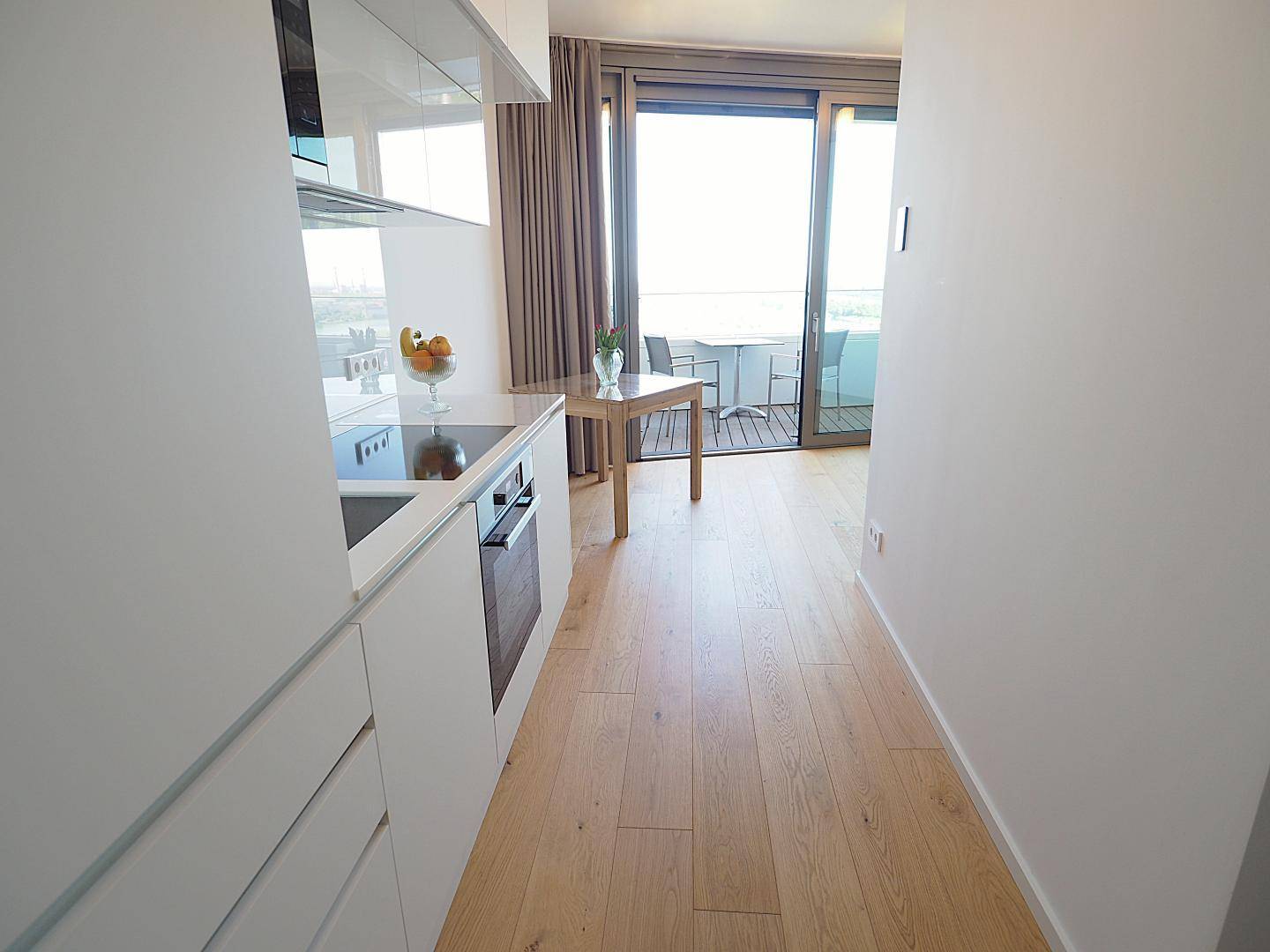 Offener Bereich mit Küchenzeile, Esstisch und Zugang zu einem sonnigen Balkon.