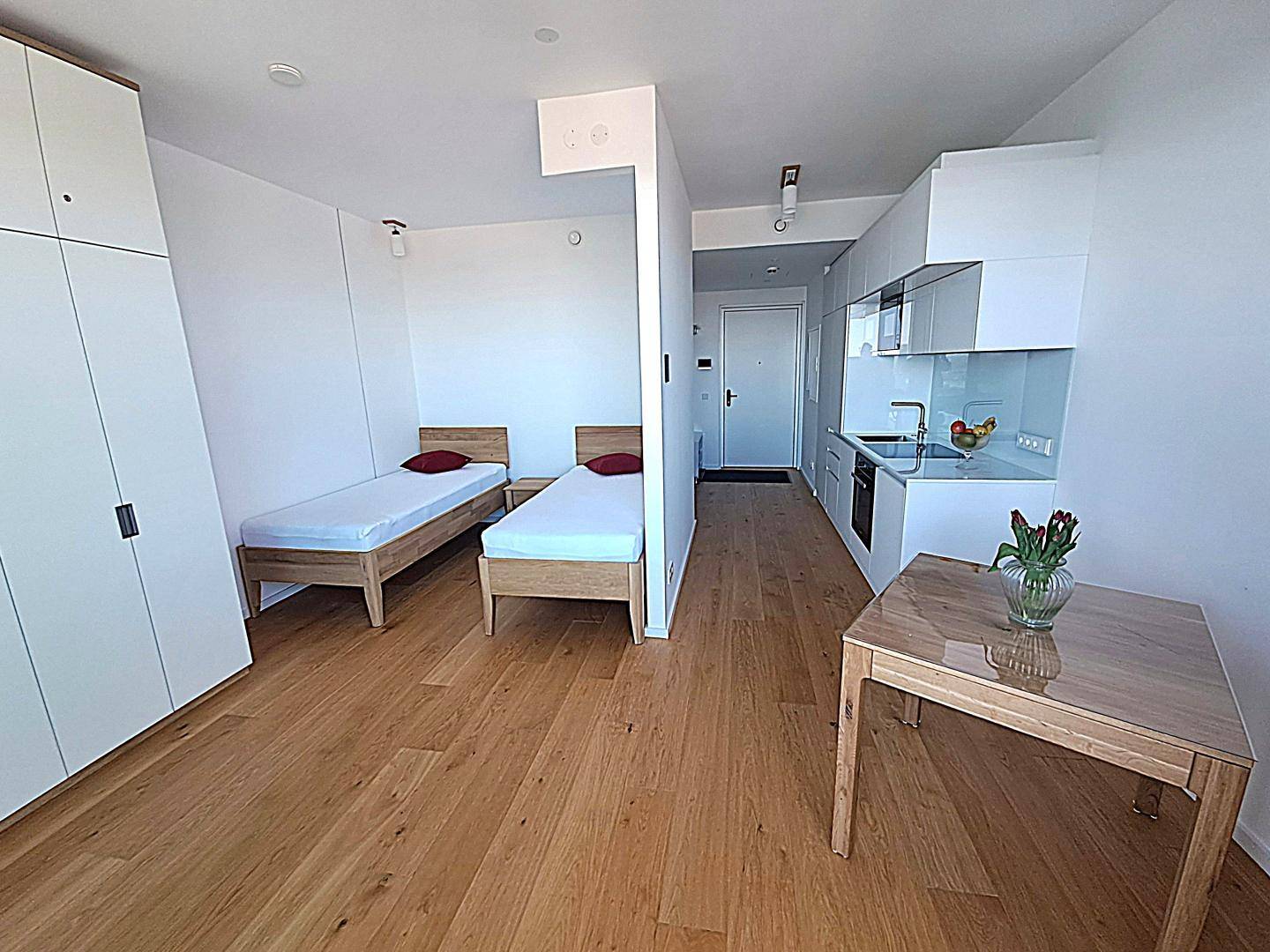 Helles Studio-Apartment mit zwei Einzelbetten, Holzboden und integrierter Küchenzeile.