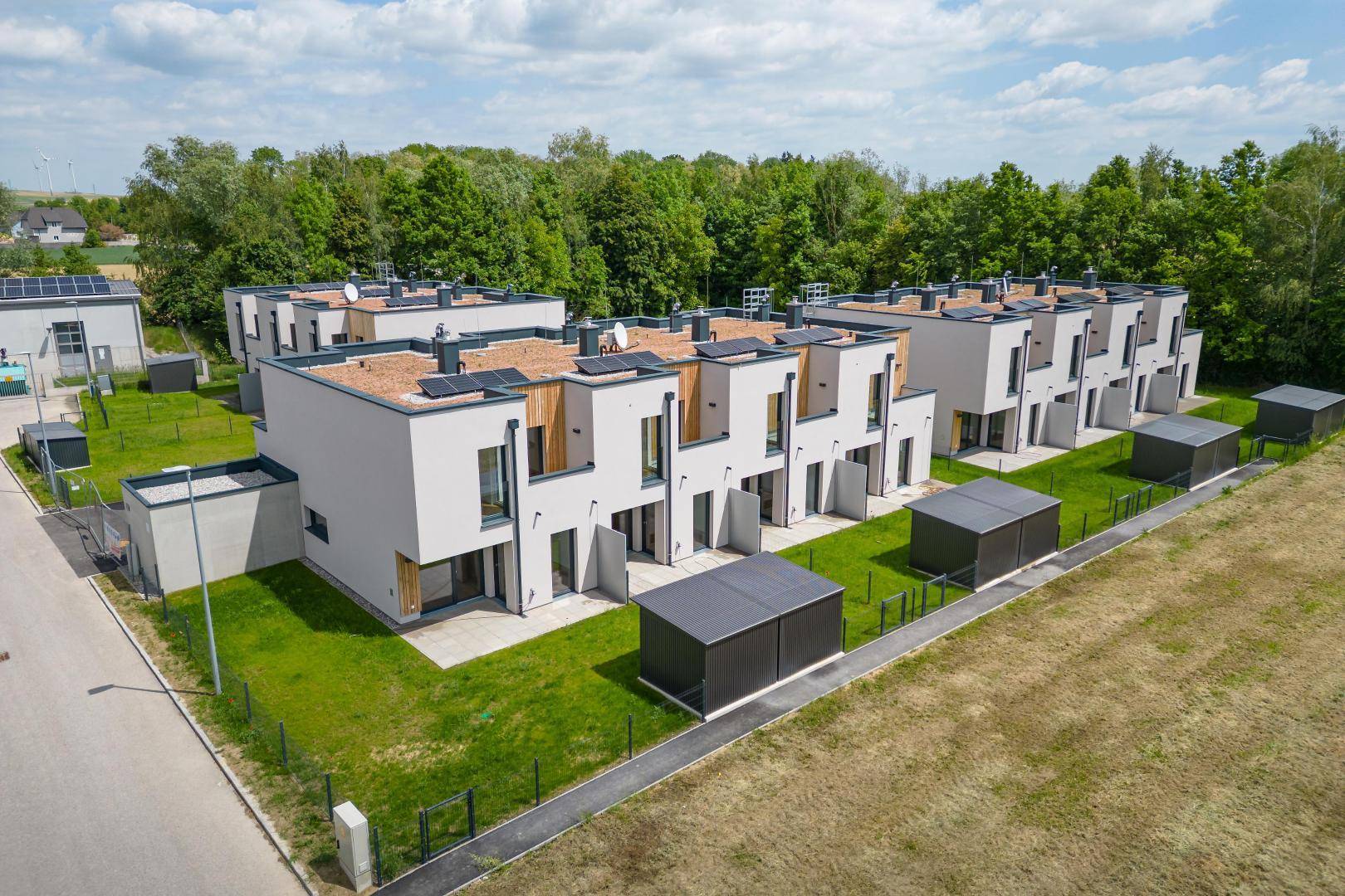 Luftaufnahme einer modernen Reihenhaussiedlung mit Photovoltaikanlagen auf den Flachdächern und viel Grünfläche.