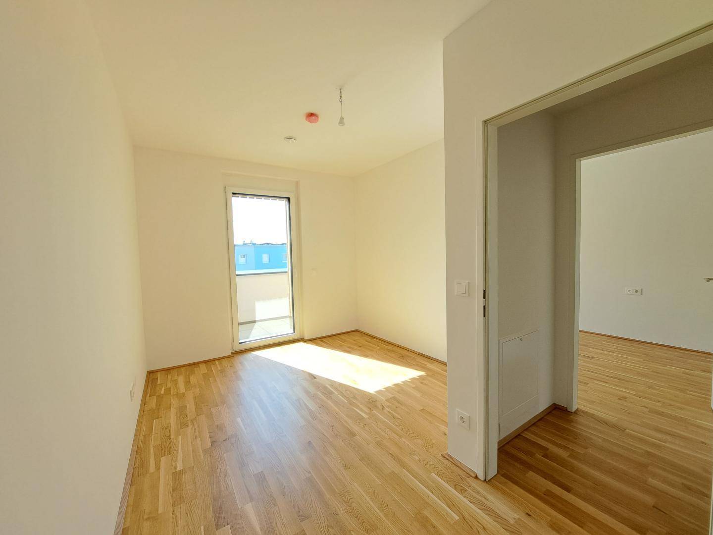 Helles Schlafzimmer mit Parkettboden und Zugang zu einem kleinen Balkon.