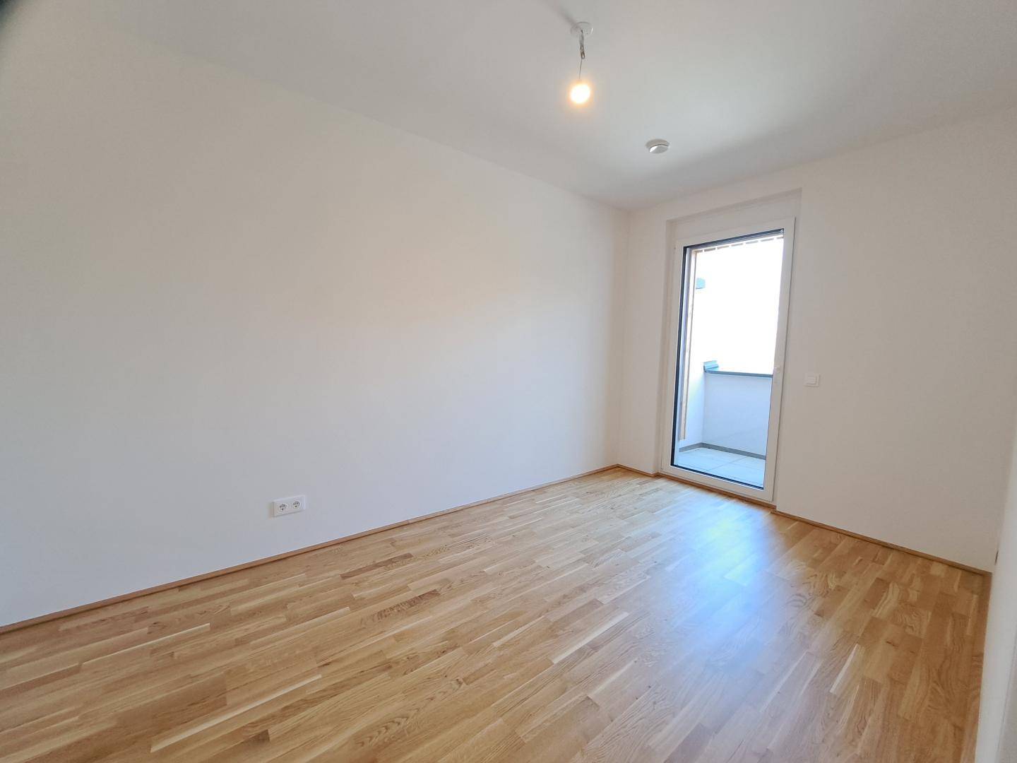 Geräumiges Schlafzimmer mit Holzboden und Balkonzugang, gut belichtet.