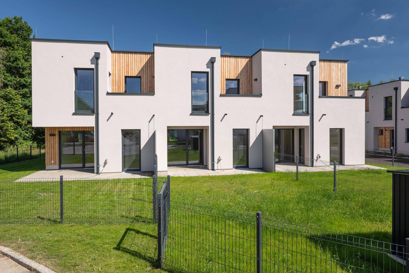 Moderne Reihenhäuser mit weißer Fassade, Holzverkleidung und gepflegten Grünflächen.
