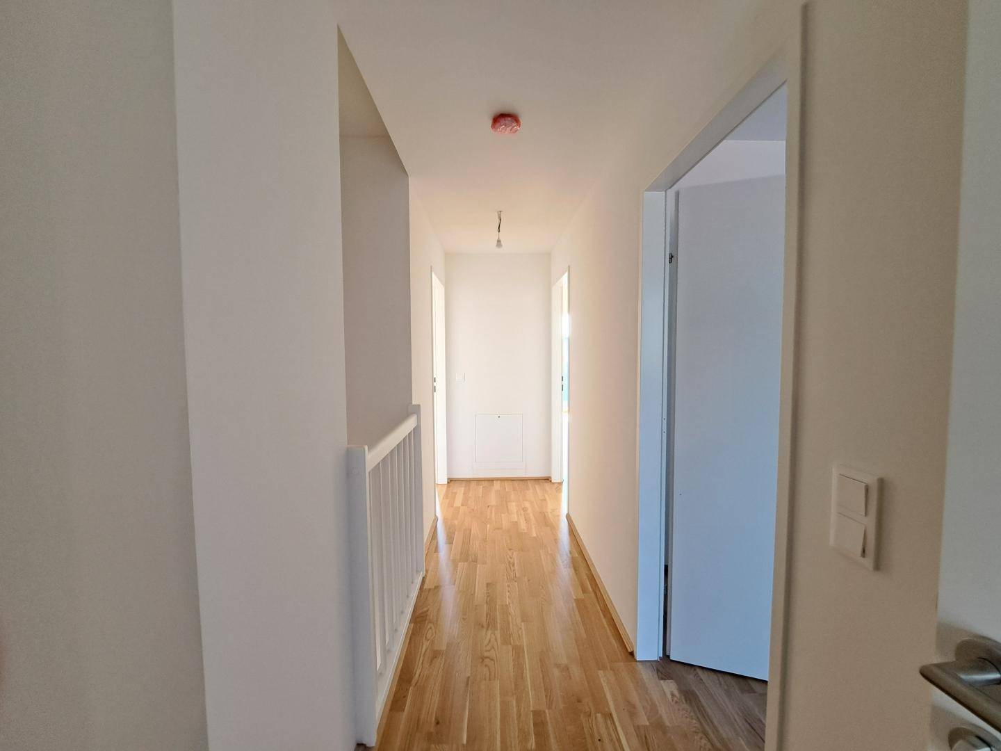 Heller Flur mit Parkettboden und weiß gestrichenen Wänden, der zu weiteren Räumen führt.