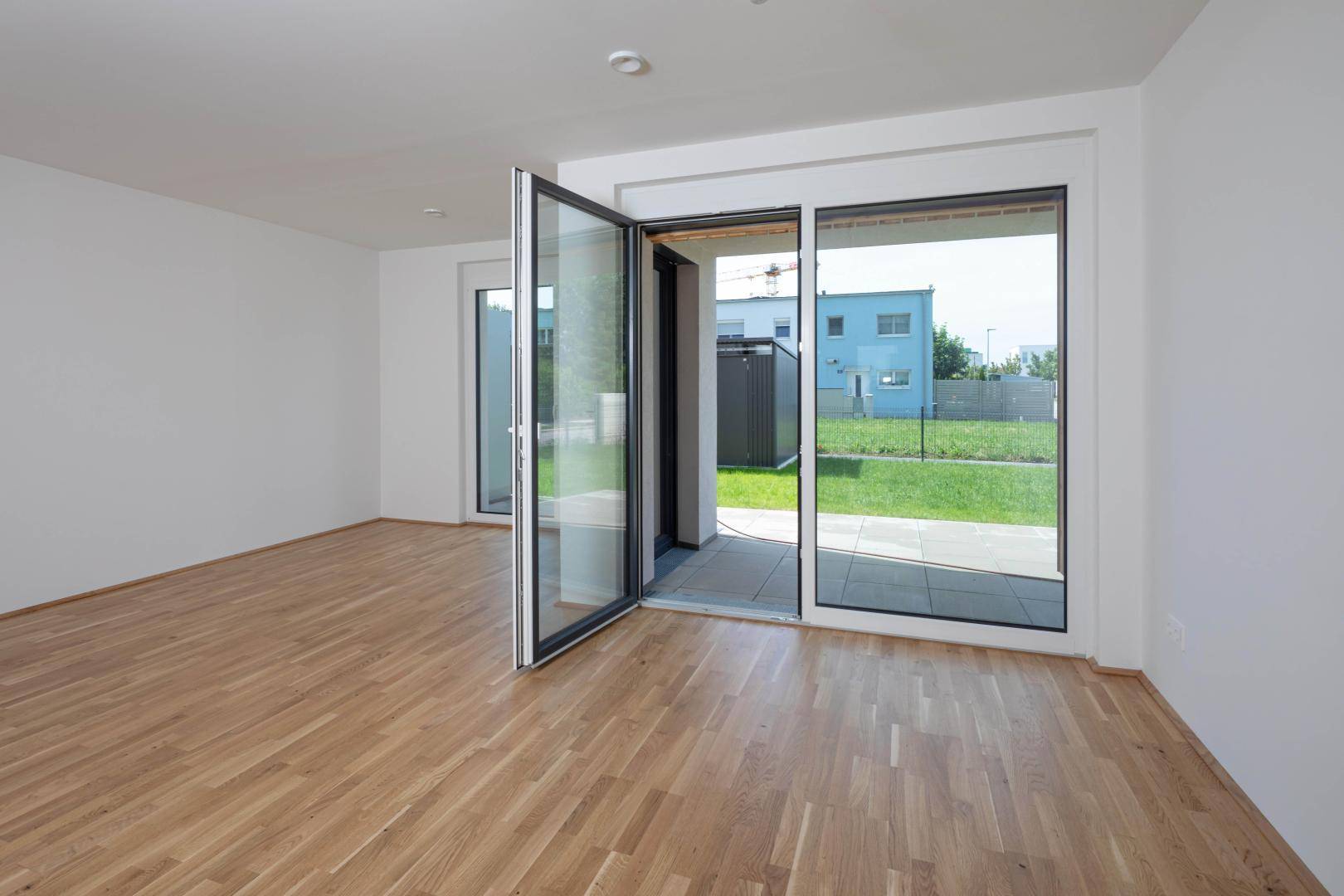 Heller Raum mit Parkettboden und großen Glasfronten, die auf eine Terrasse und den Garten führen.