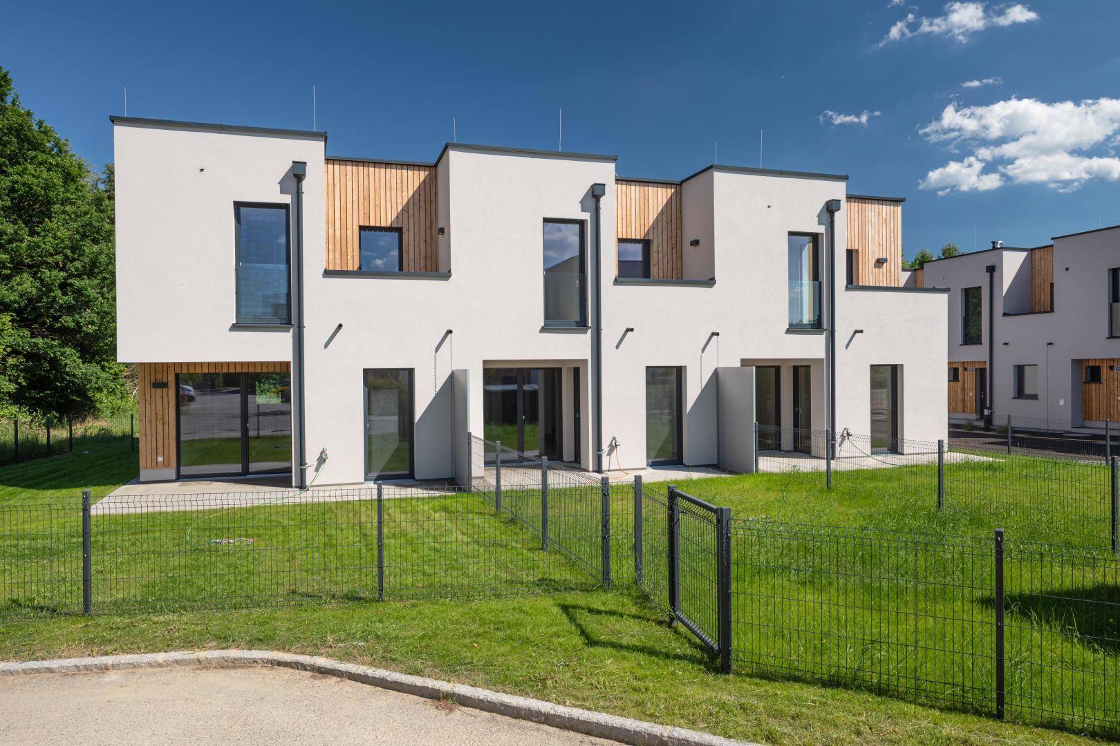 Moderne Reihenhäuser mit weißer Fassade, Holzverkleidung und kleinen privaten Gärten.