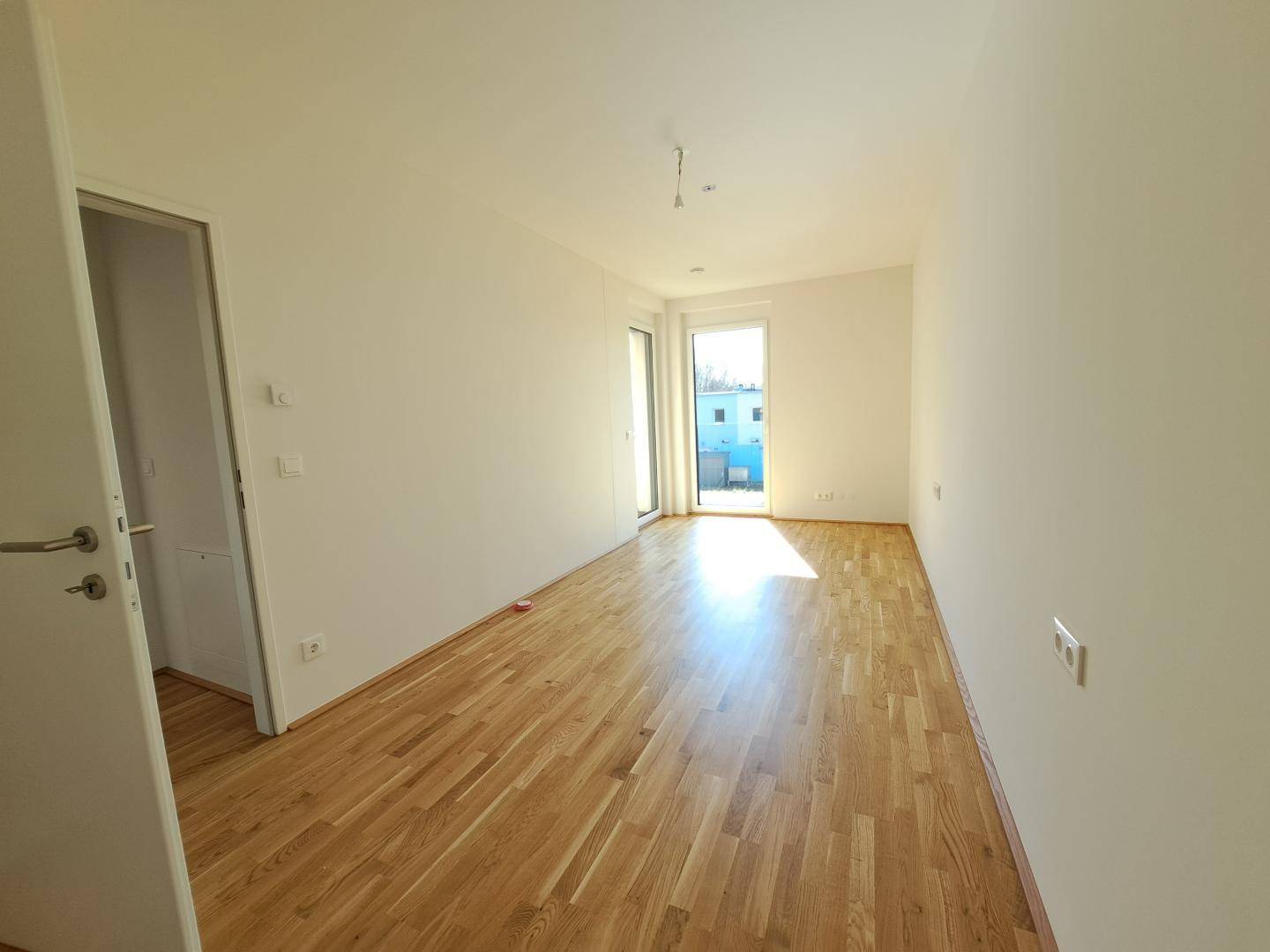 Heller Raum mit Parkettboden und Zugang zu einem Außenbereich, ideal als Schlaf- oder Arbeitszimmer.