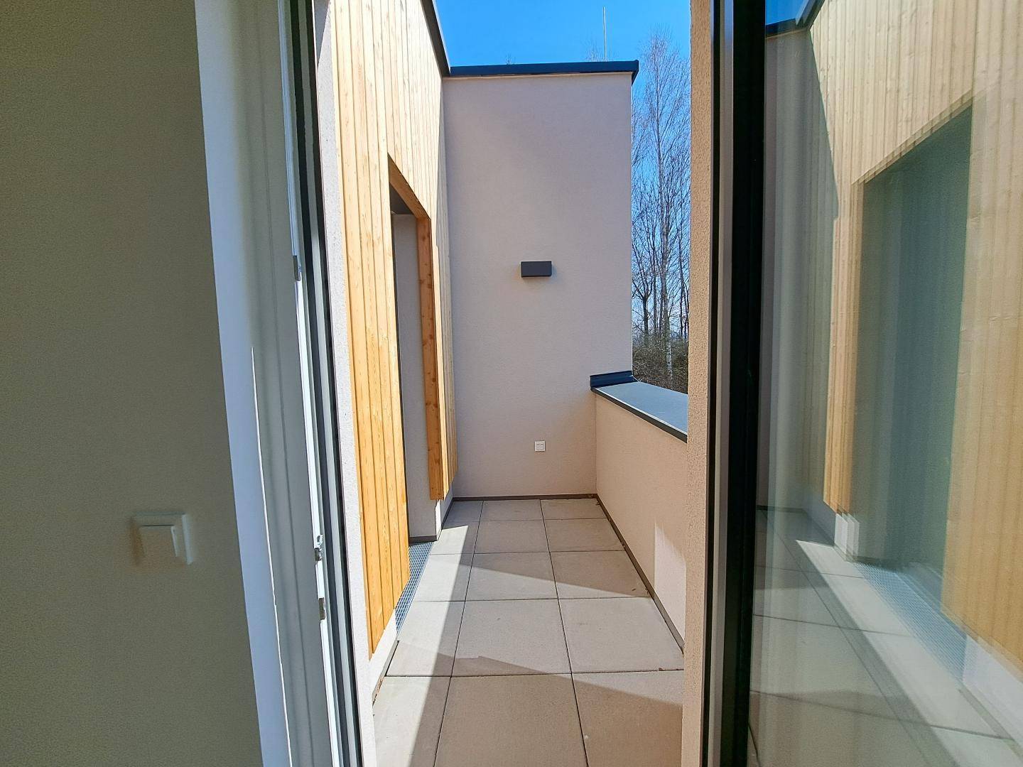 Kleiner, gefliester Balkon mit Holzverkleidung und Blick ins Freie.
