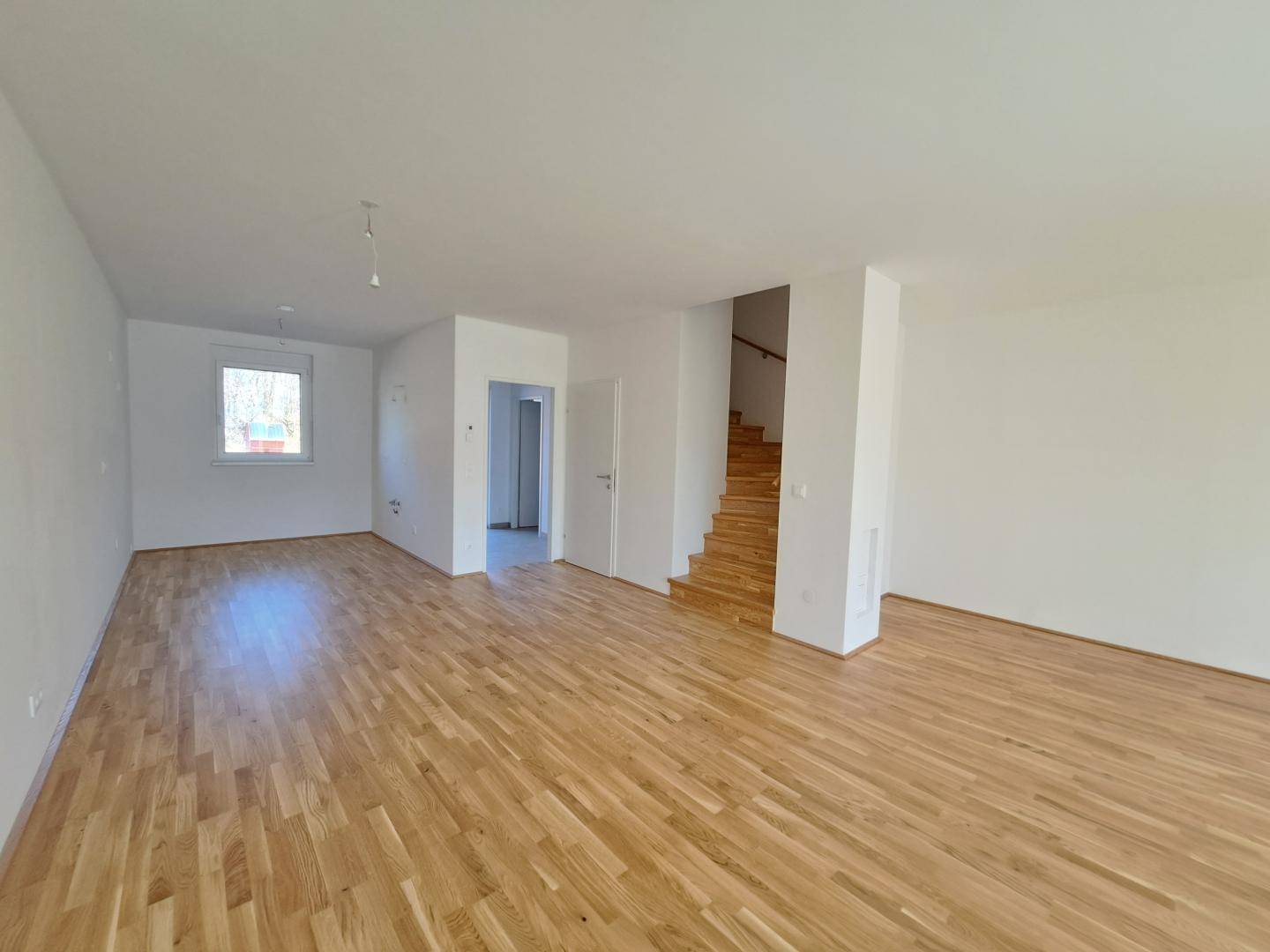 Geräumiges Wohnzimmer mit hellem Parkettboden und offenem Zugang zu den Holztreppen.