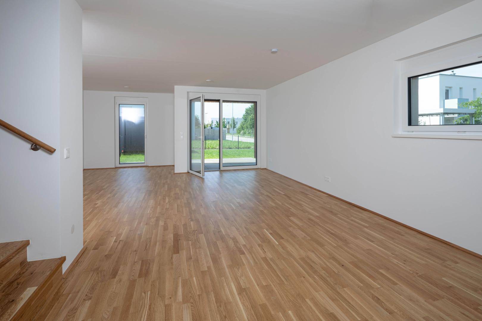 Helles, leeres Wohnzimmer mit Eichenparkettboden und großen Fenstern zum Garten.