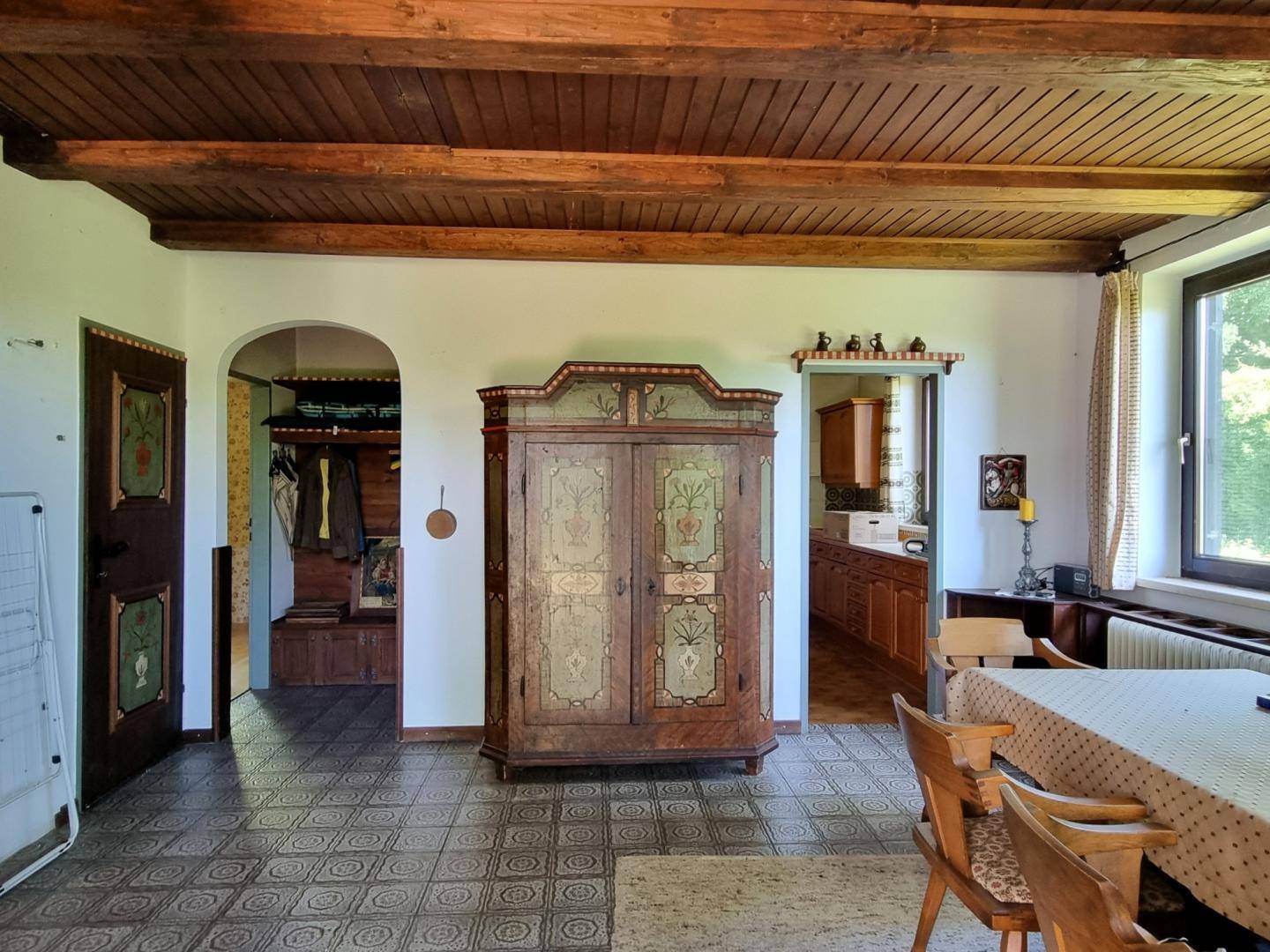 Essbereich mit kunstvollem Holzschrank, Fliesenboden und einem Durchgang zu einem weiteren Raum.
