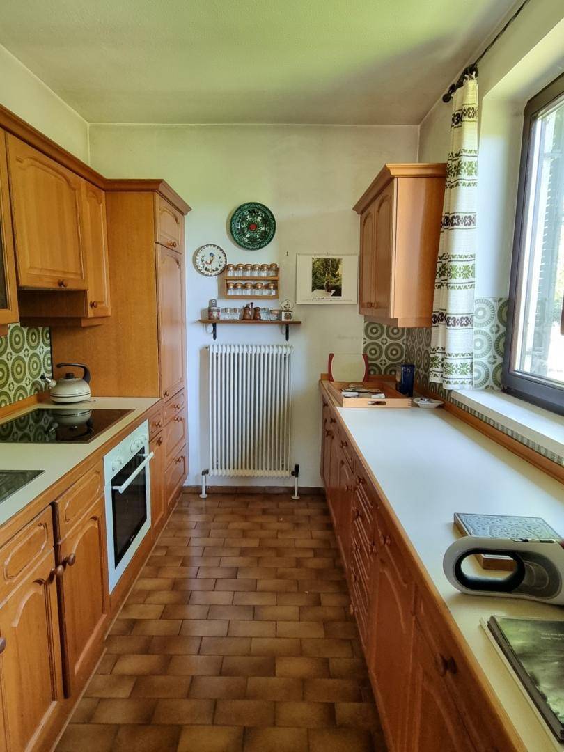 Küche mit Holzschränken, weißen Arbeitsplatten und einem Fenster, das viel Tageslicht hereinlässt.