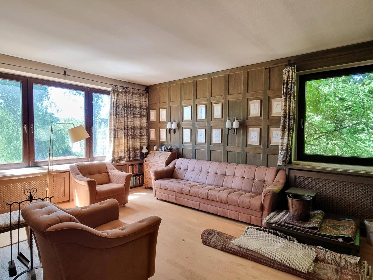 Gemütliches Wohnzimmer mit Holztäfelung, großen Fenstern und bequemen Vintage-Sitzmöbeln.