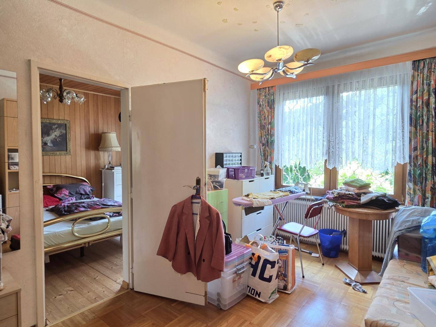 Schlafzimmer mit Holzboden, gemusterter Tapete und Zugang zu einem weiteren Raum.