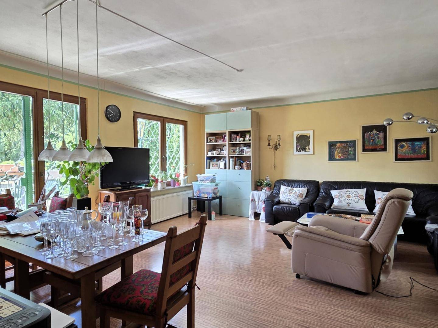 Geräumiger Wohn- und Essbereich mit Holzfußboden, großen Fenstern und gelben Wänden.